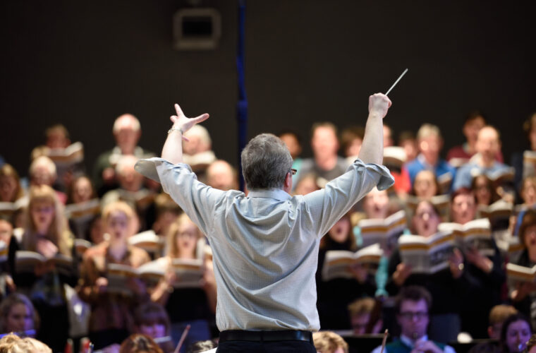 A conductor is conducting a choir and orchestra in a concert hall.