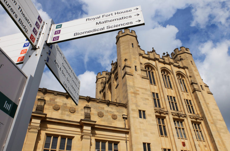 A sign pointing to places in the four cardinal directions. The sign is in front of a neo-gothic building.